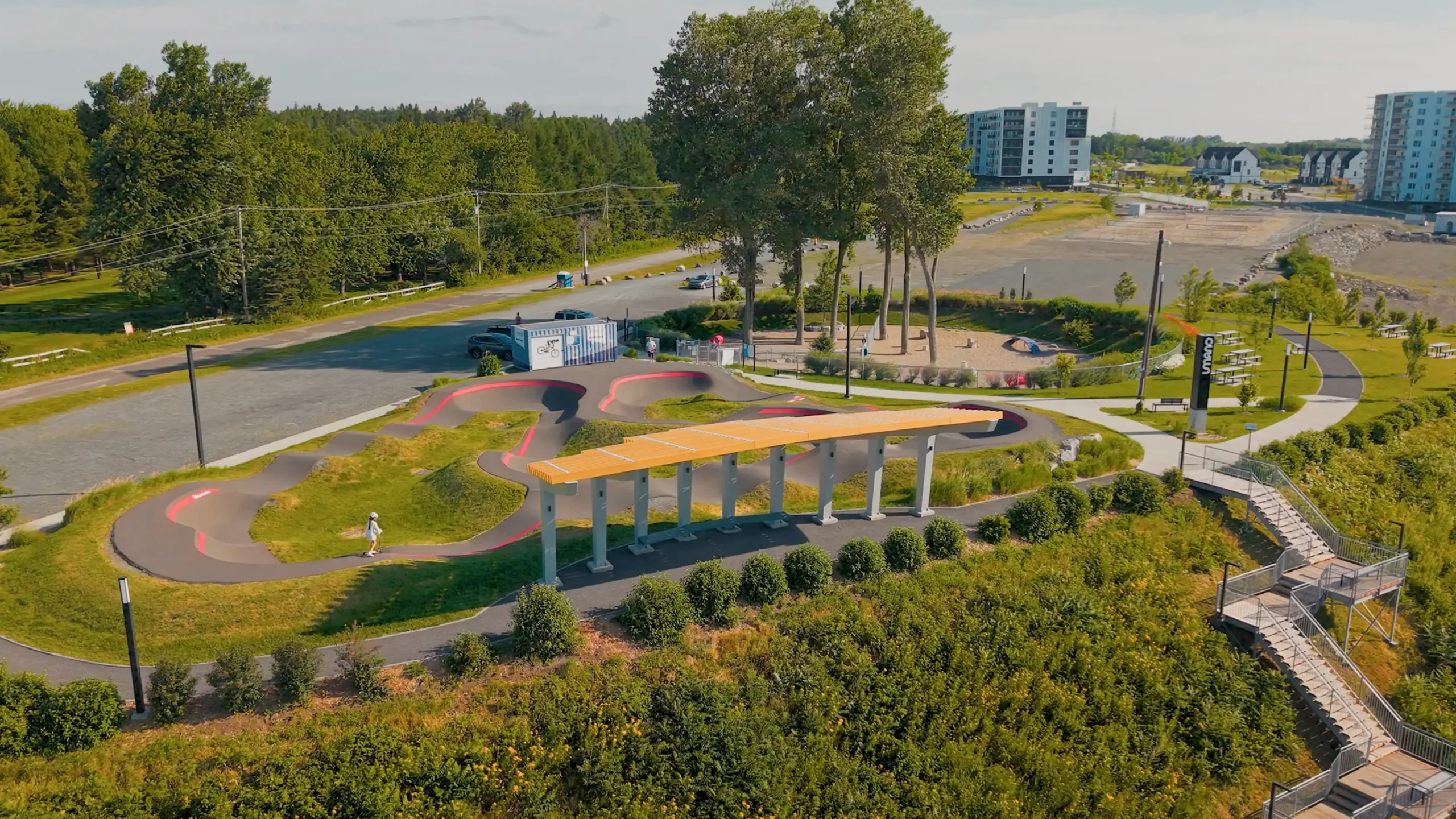 Piste cycliste urbaine avec structures modernes et espaces verts entourant un parc public.